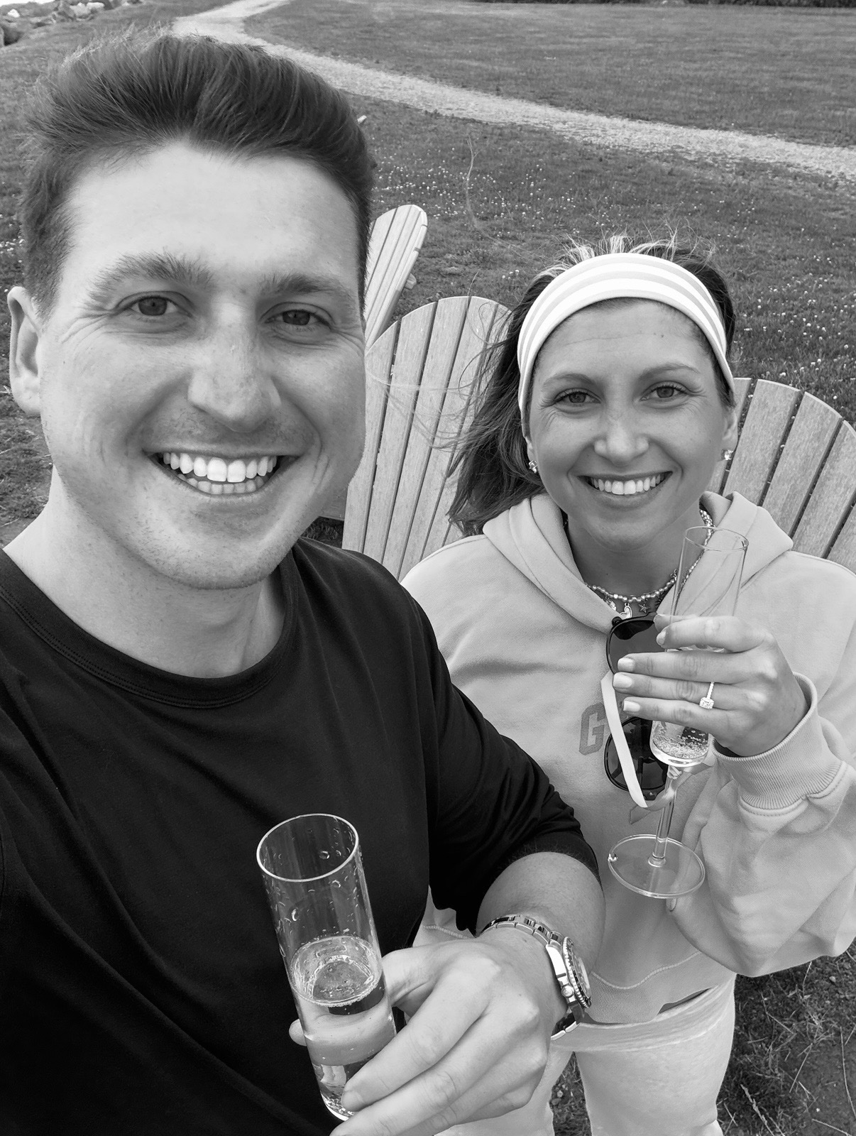 Selfie of Andrew and Jenna toasting with champagne flutes in Adirondack chairs