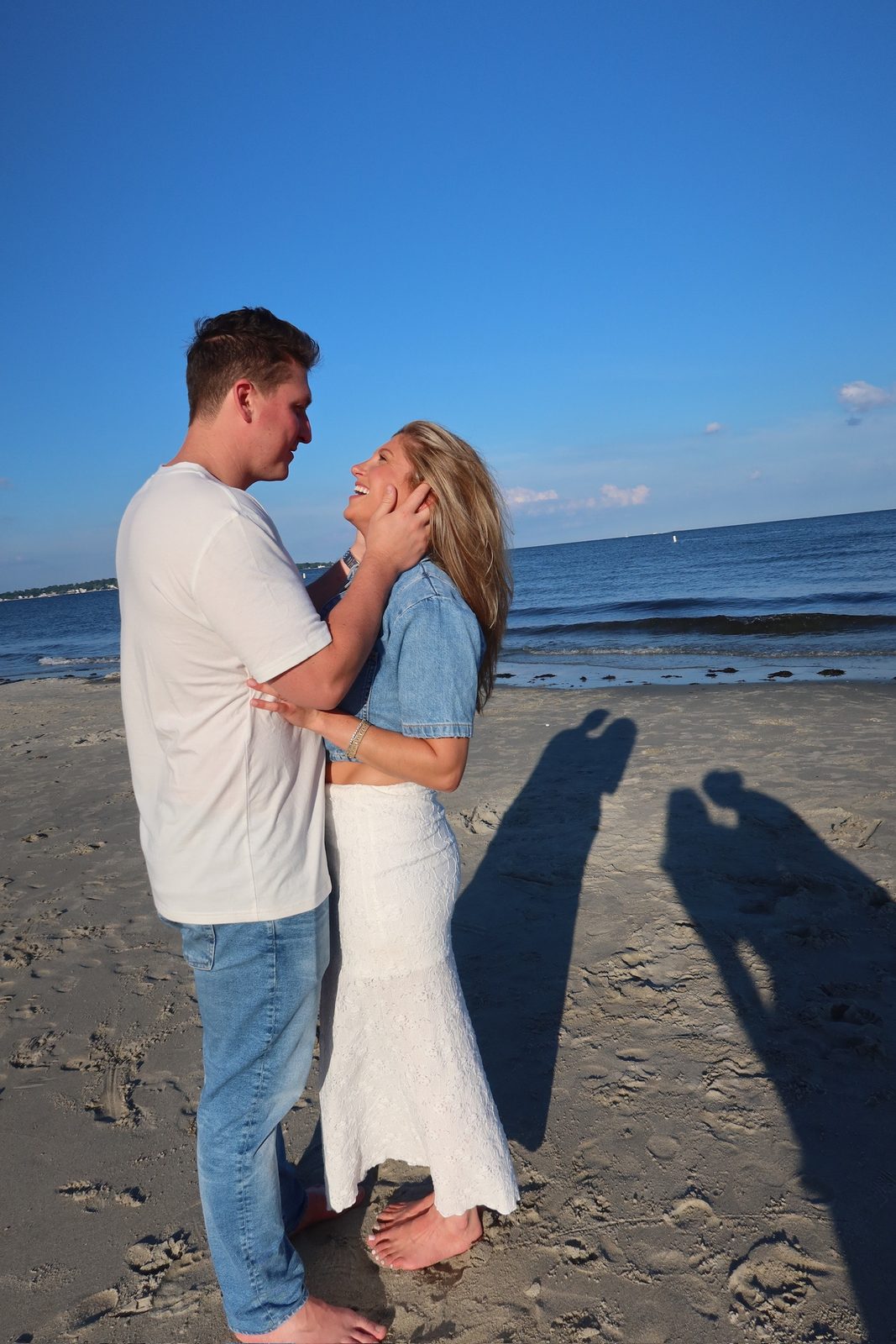 Andrew holding Jenna's face as she laughs on the beach