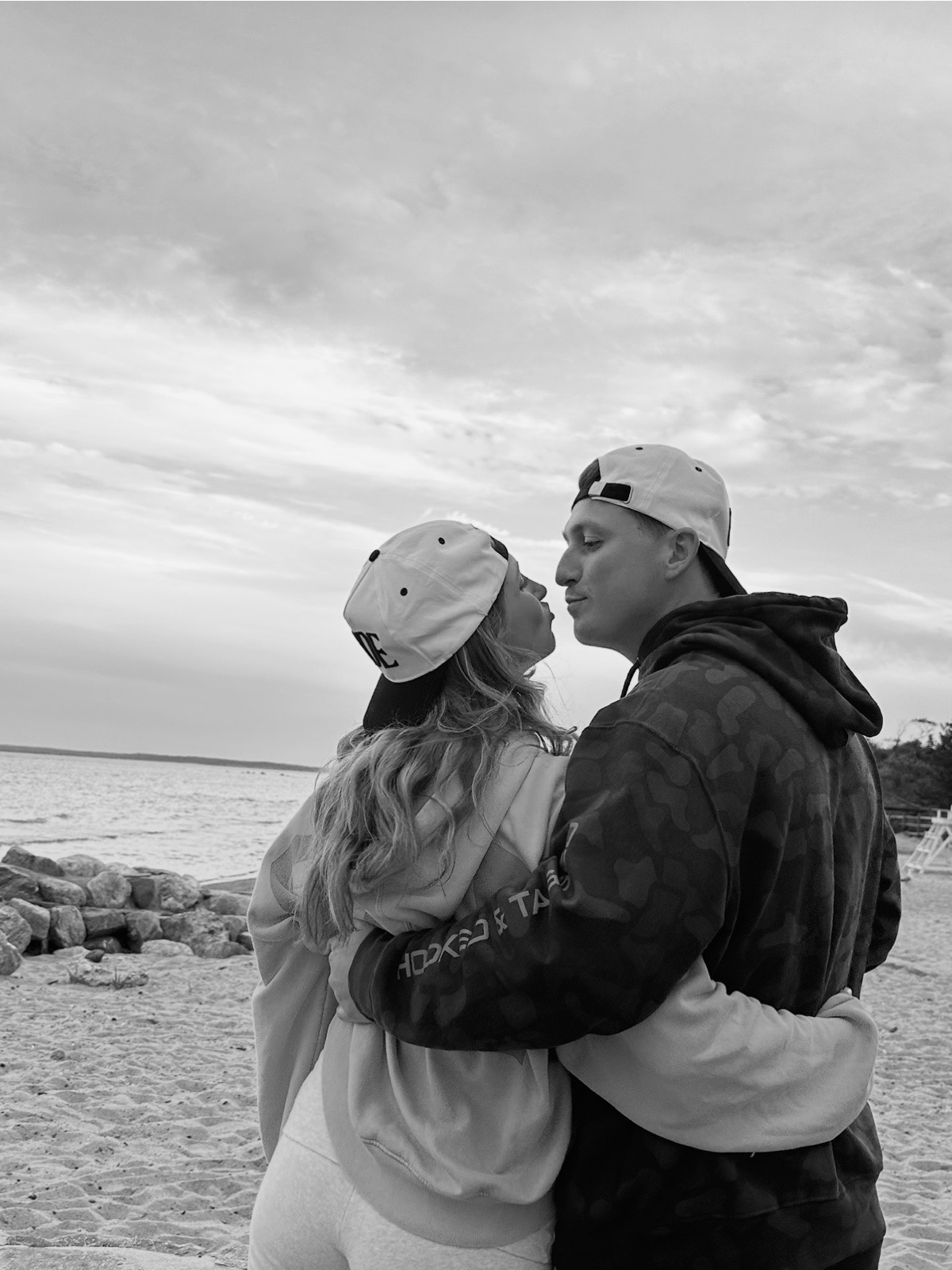 Andrew and Jenna kissing on the beach in backwards caps