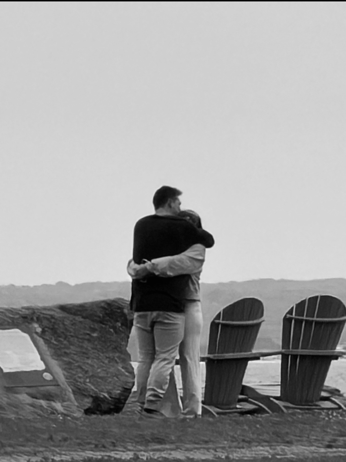 Andrew and Jenna embracing by the water next to Adirondack chairs